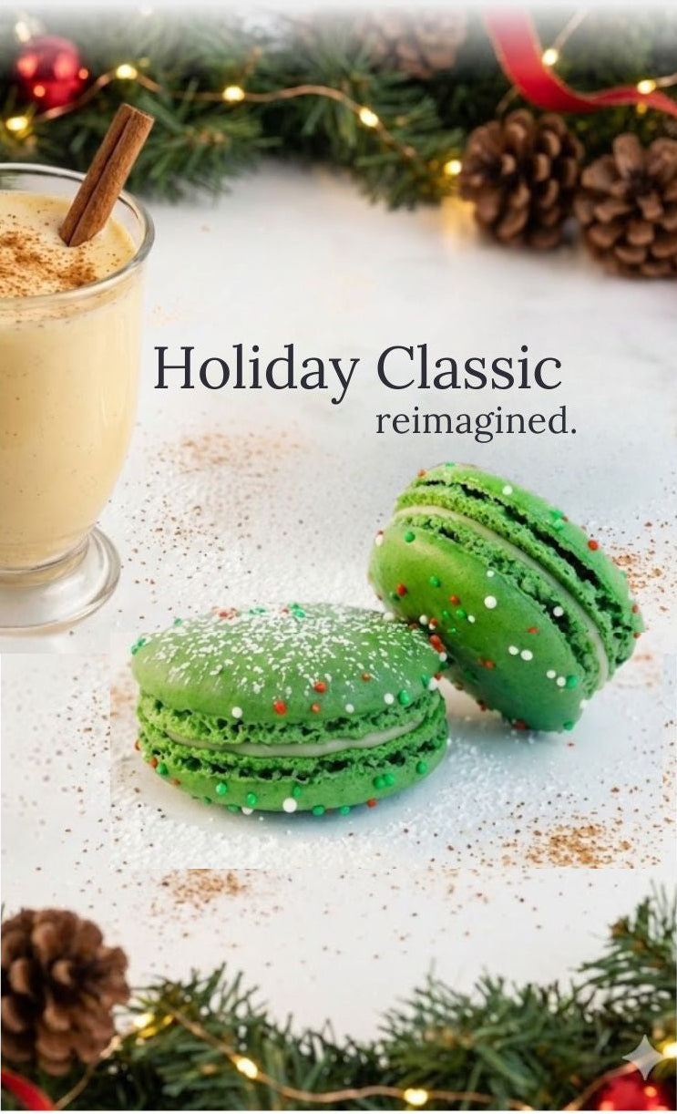 Green macarons with festive decorations on a white surface with a glass of eggnog and Christmas decorations in the background.